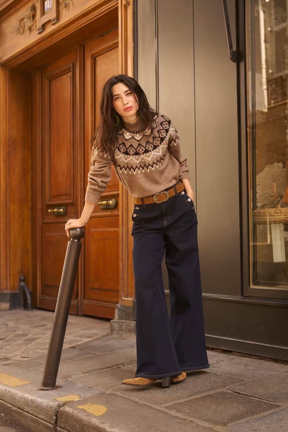 Model in a patterned knit jumper and navy trousers, leaning in a doorway on a European street