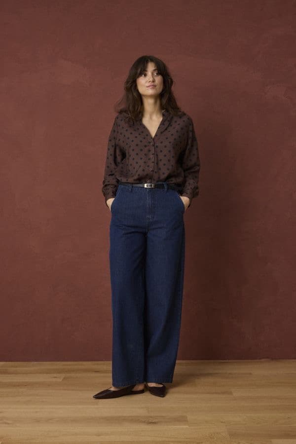 Model in a dark printed blouse and navy denim against a plain studio background