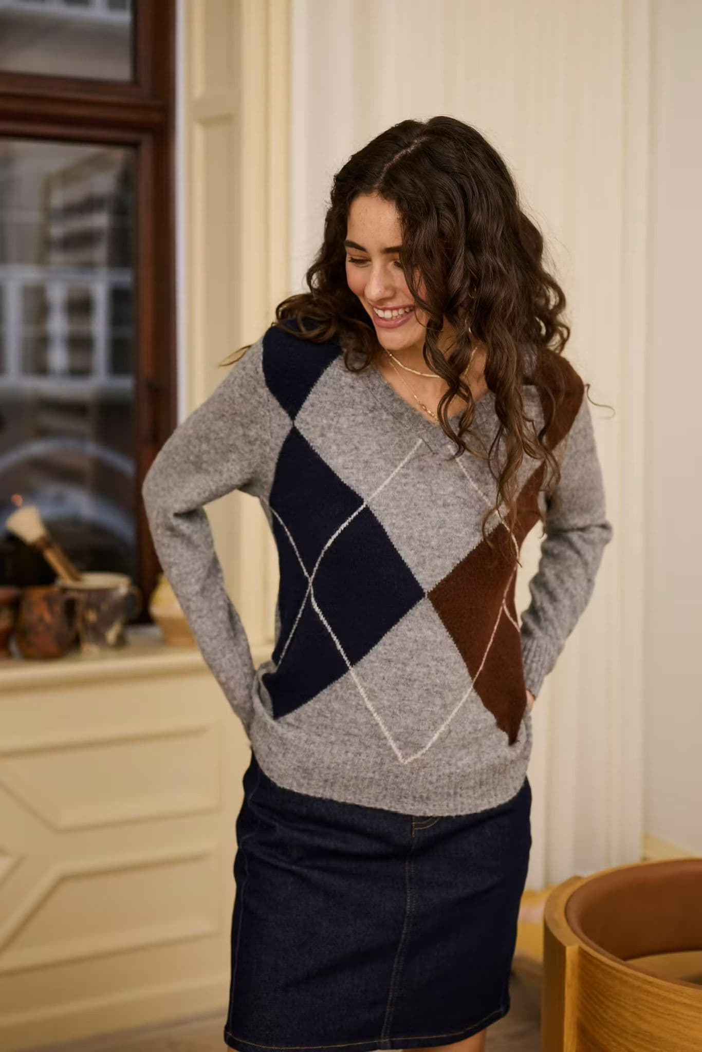 Model in an argyle-pattern knit and midi skirt standing in a wooden doorway