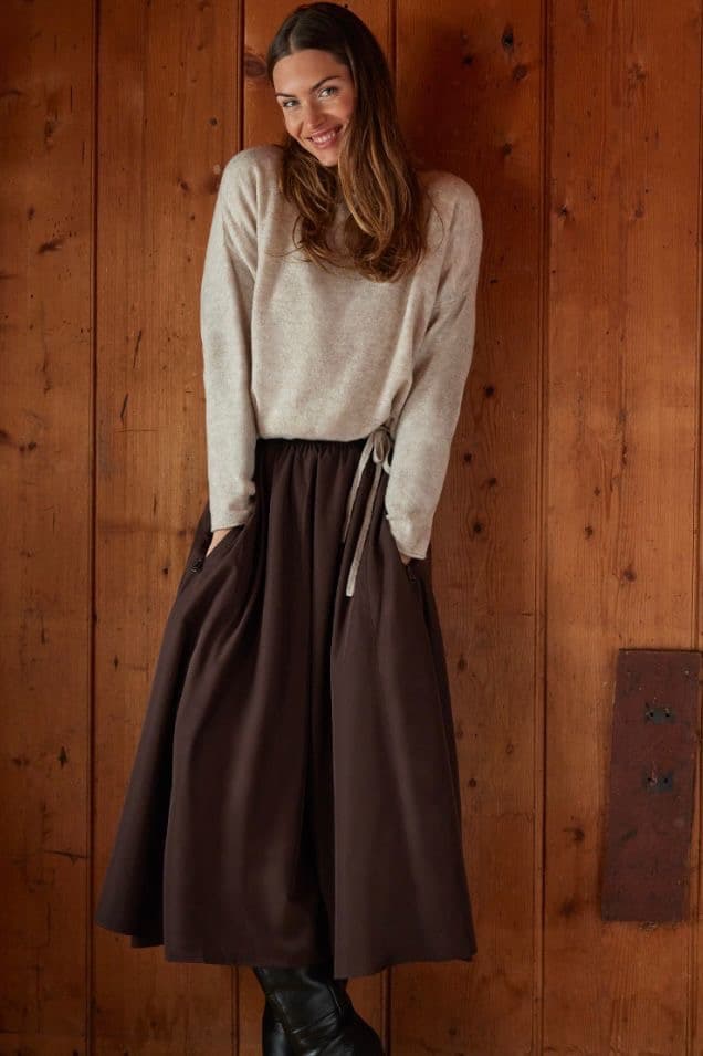 Model in a cream sweater and brown midi skirt against a carved wooden door