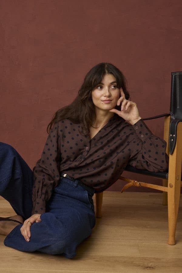 Model in a dark patterned blouse seated against a warm wood-panelled interior