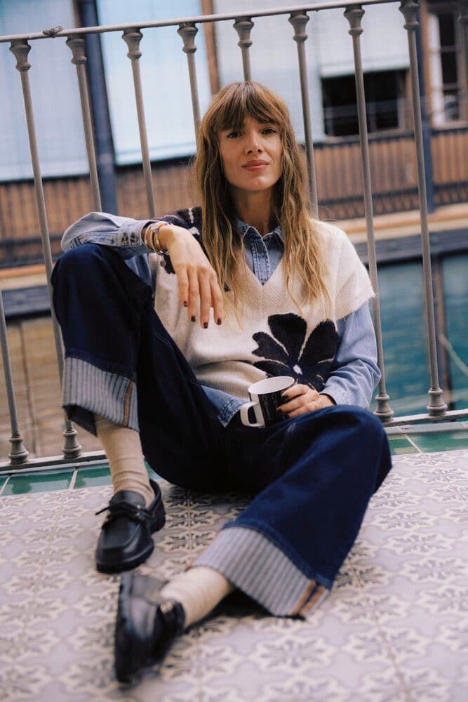 Model in a cream sweater and navy trousers seated on a stone ledge in a courtyard