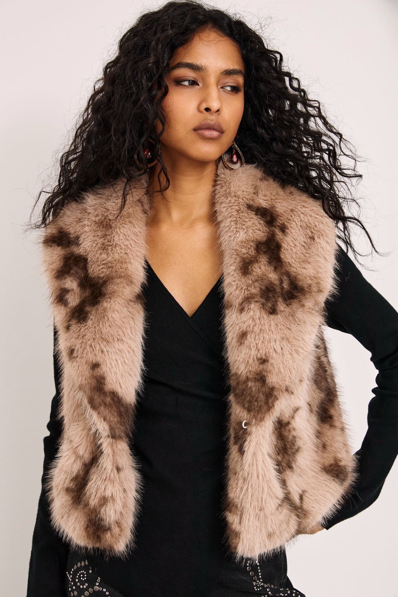 Model in a camel faux fur gilet over a black top, studio background