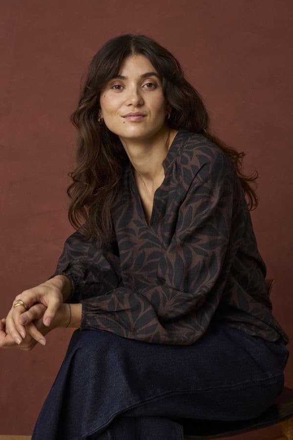Model seated wearing a dark floral print blouse against a plain studio background