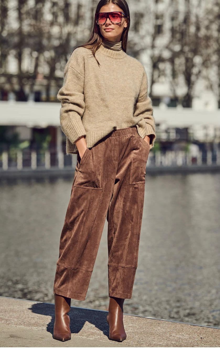 Model in a cream sweater and brown cord trousers beside a river