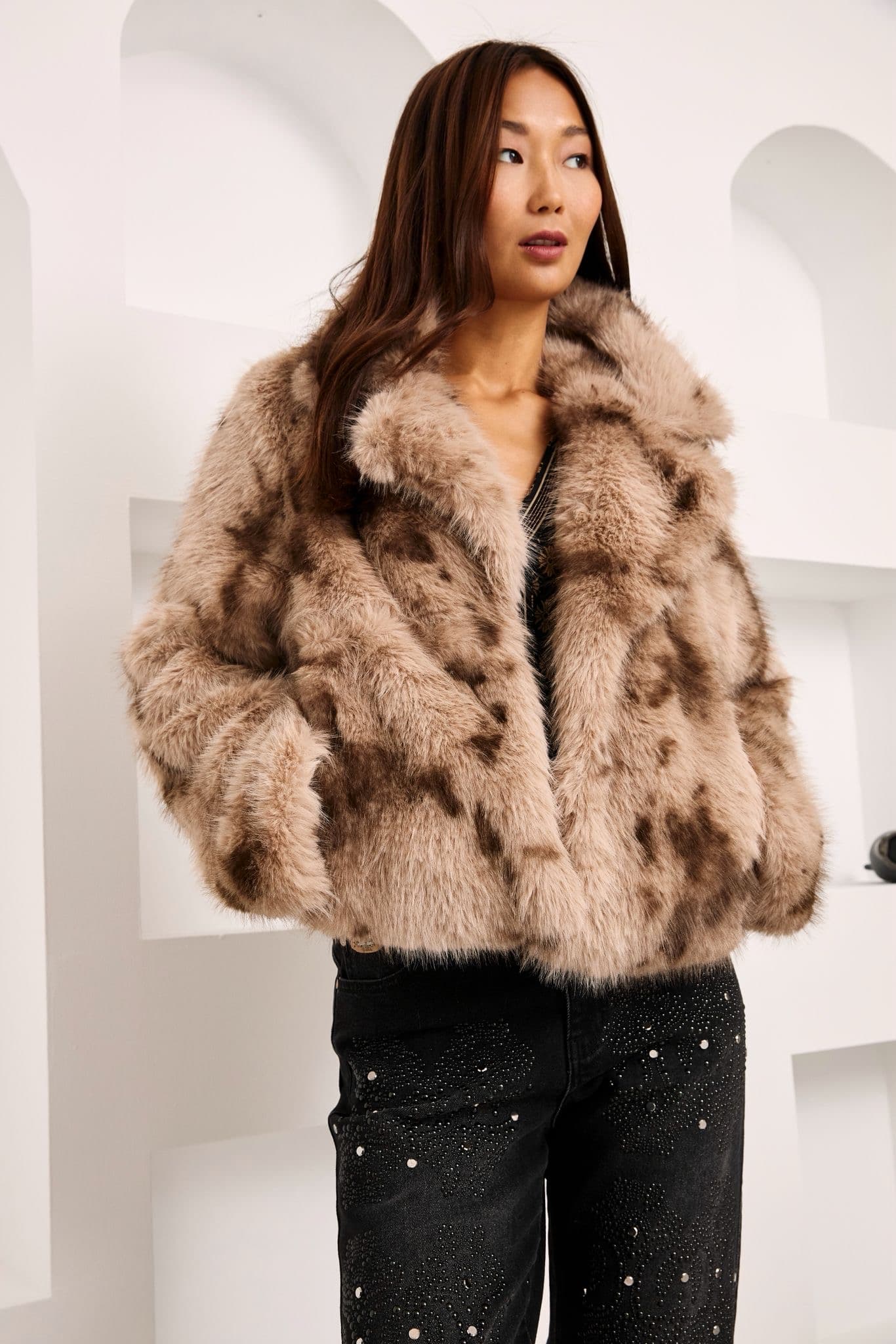 Model in a camel faux fur jacket over dark sequined trousers, studio background