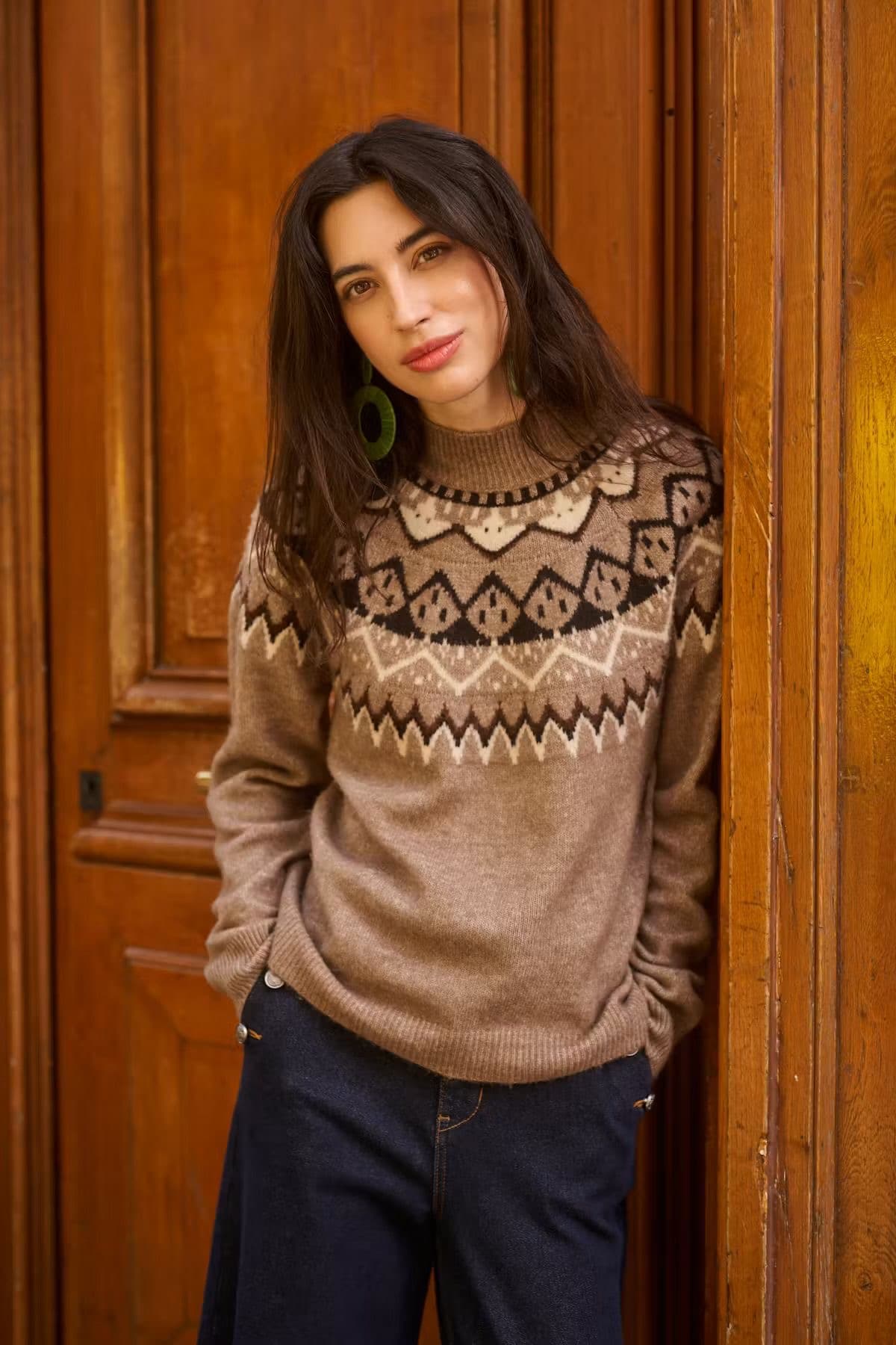 Model in a brown and tan fair isle patterned jumper, standing in a wooden doorway