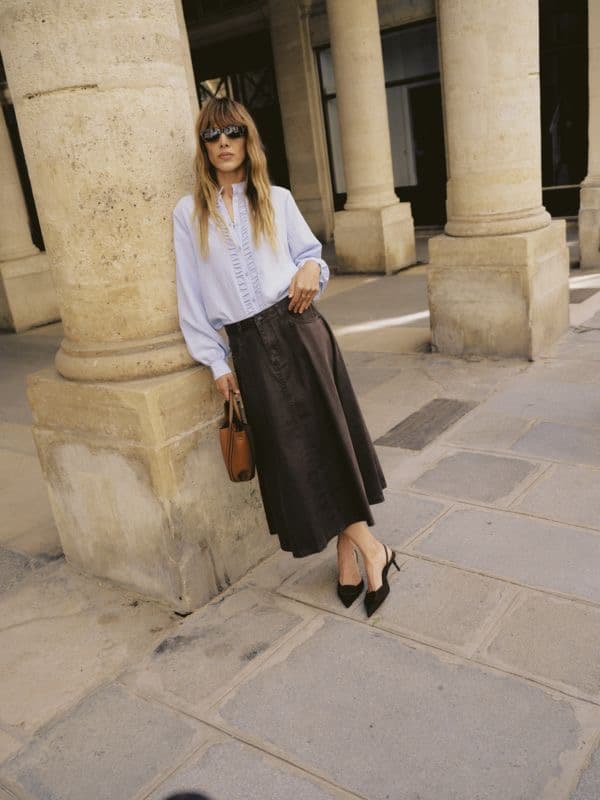 Model in a white blouse and black skirt standing between street pillars