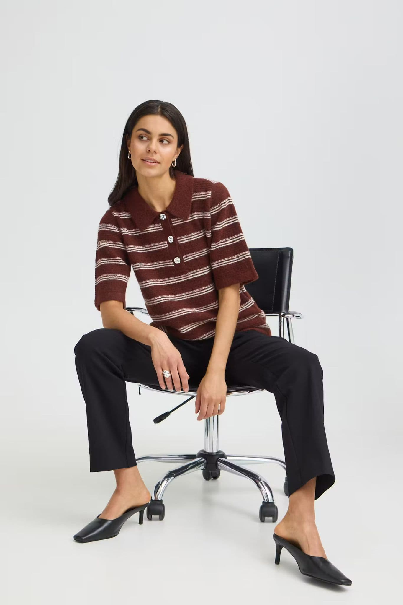 Model seated on an office chair wearing a burgundy and cream striped shirt