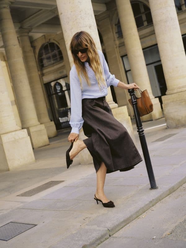 Model in a white blouse and pleated brown skirt on a city street