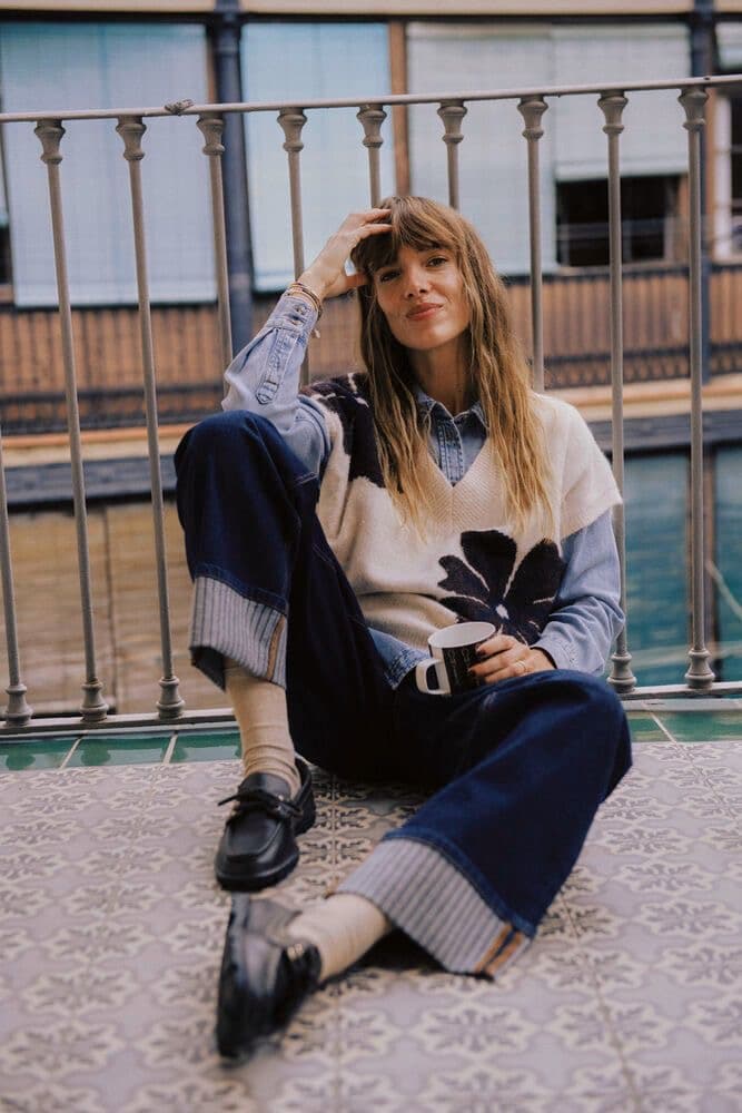 Model seated on a street ledge in a patterned cream and blue sweater