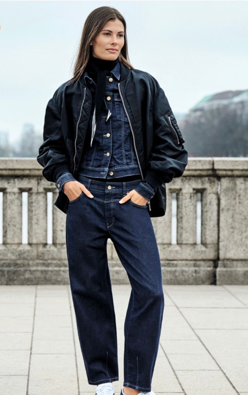 Model in a navy quilted puffer jacket and wide trousers on a mountain terrace