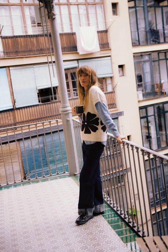 Model in a cream sweater seated on a street railing