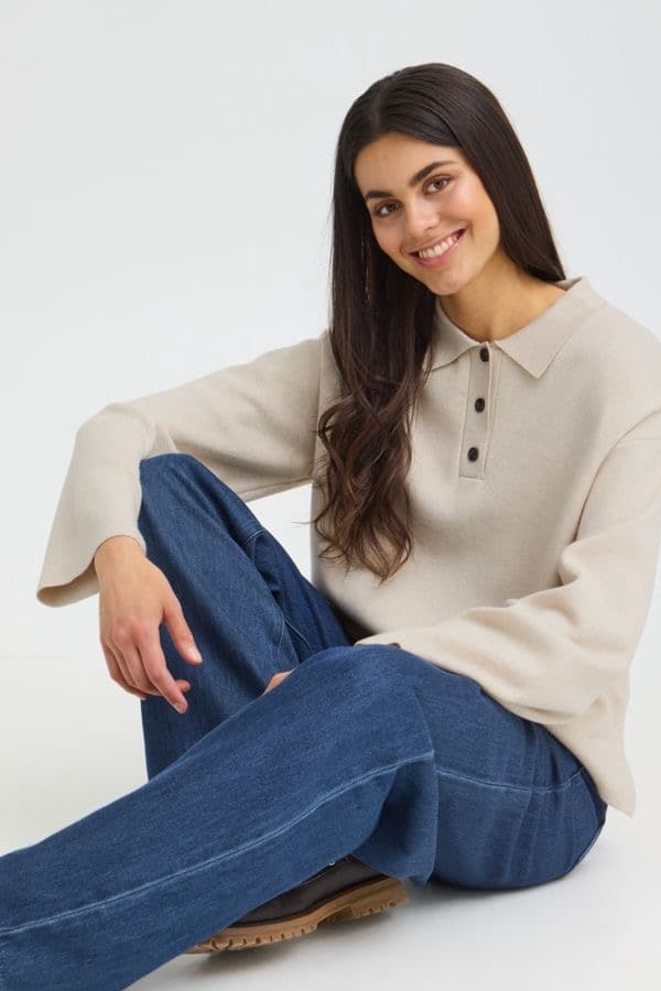 Model seated wearing a cream popover sweater and wide-leg denim, studio background