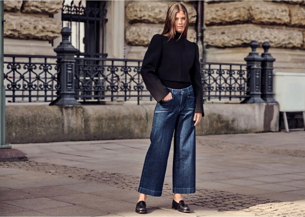 Model walking on a cobbled European street in a navy top and wide-leg dark denim