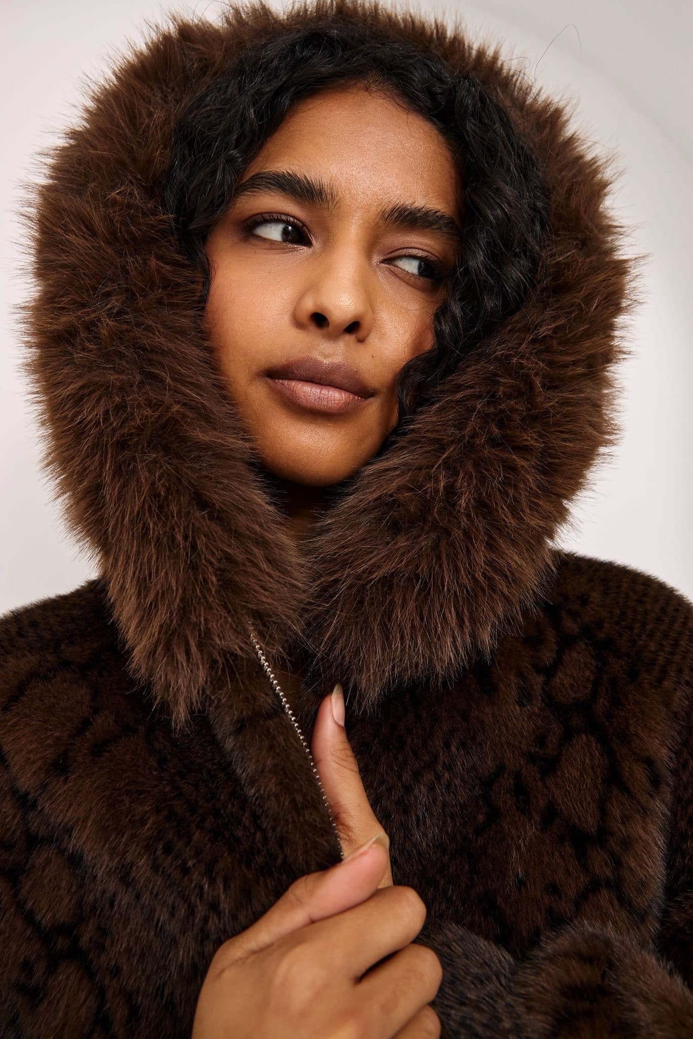 Close portrait of a model wearing a dark brown faux fur hooded jacket